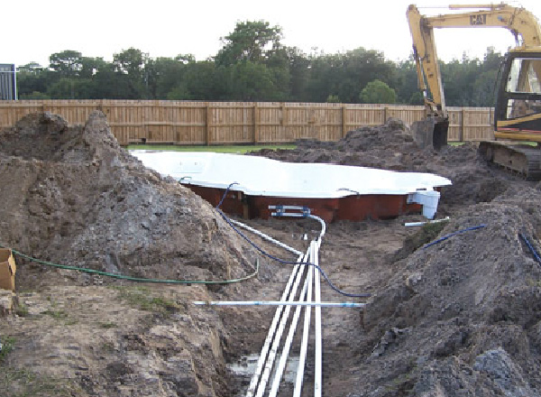 Fiberglass pool shell being placed into a hole in backyard