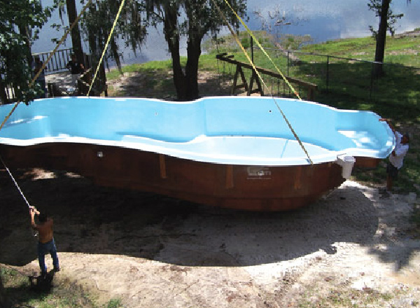 Fibeerglass pool shell being lowered into a yard