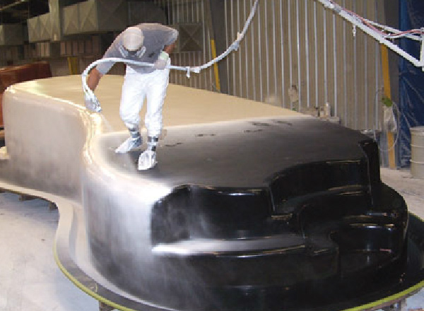 Worker spraying a coating onto the shell of a fiberglass pool during manufacturing