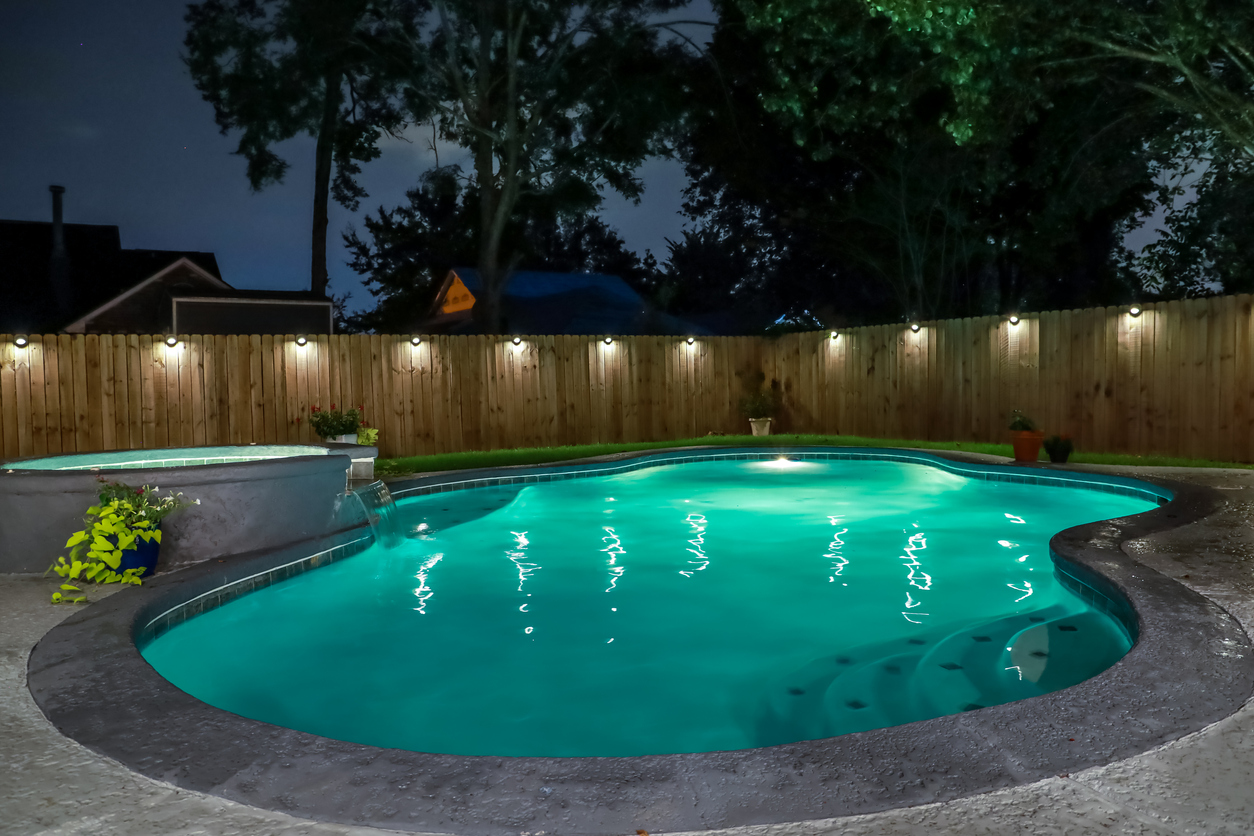 A backyard swimming pool and Hot Tub hot tob at night with solar lights around the fence for privacy and illumination.